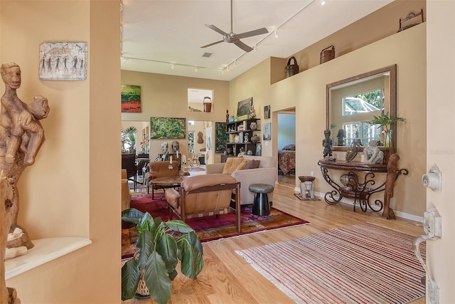 living area with a ceiling fan, rail lighting, wood finished floors, and baseboards