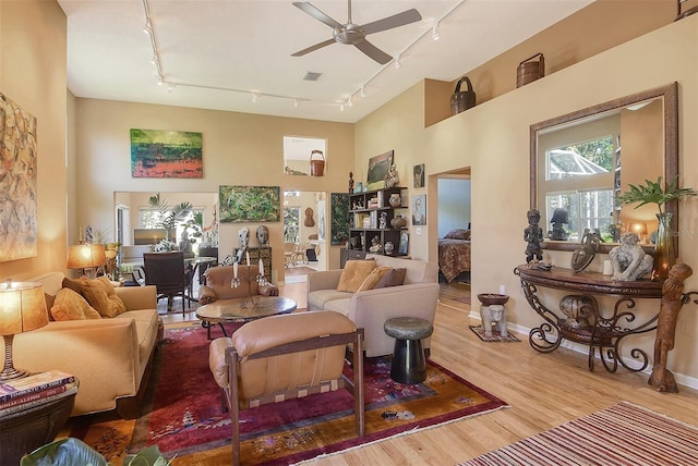 living area with a ceiling fan, wood finished floors, baseboards, a high ceiling, and track lighting