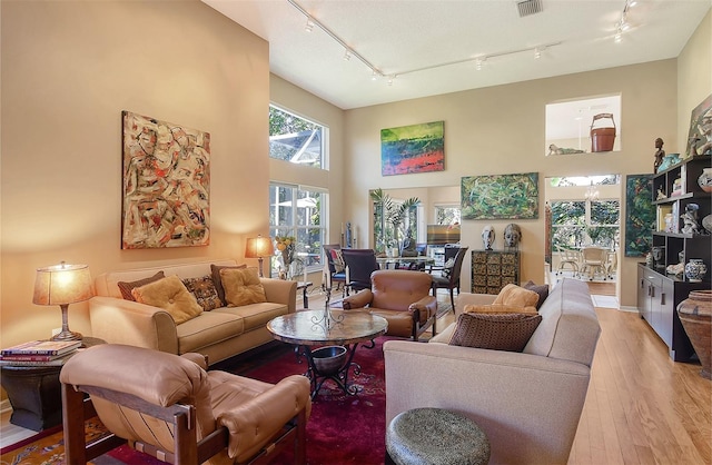 living room with light wood finished floors, visible vents, track lighting, and a towering ceiling