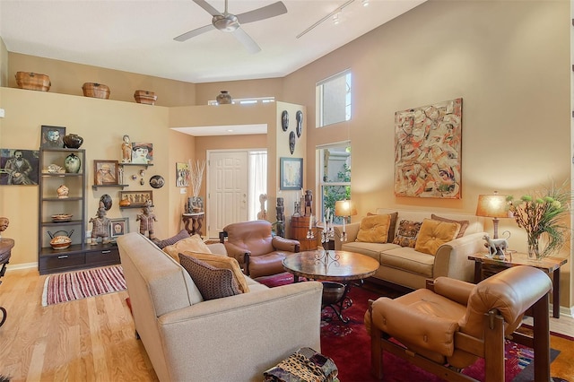 living area featuring a towering ceiling, baseboards, light wood finished floors, and ceiling fan