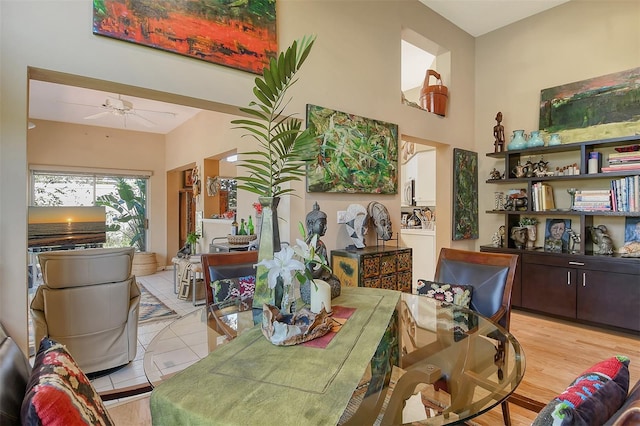 dining space with ceiling fan, light wood-type flooring, and a towering ceiling