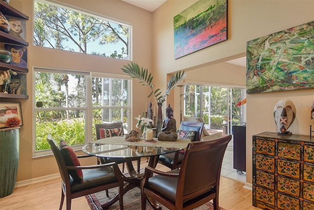 dining room featuring a high ceiling, light wood-style floors, and baseboards