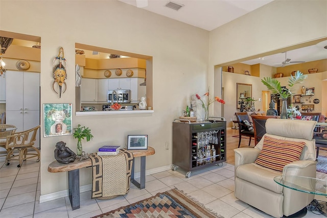 living area featuring light tile patterned flooring, a ceiling fan, visible vents, and baseboards