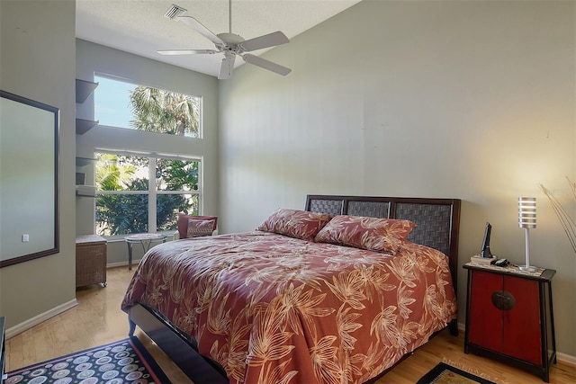 bedroom with visible vents, baseboards, a towering ceiling, wood finished floors, and a textured ceiling