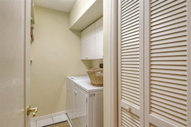 laundry area with washing machine and dryer, light tile patterned flooring, cabinet space, and baseboards