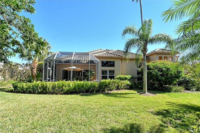 back of property featuring a tiled roof, glass enclosure, a yard, and stucco siding