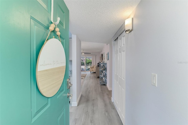 corridor with light wood-style floors, a textured ceiling, and baseboards