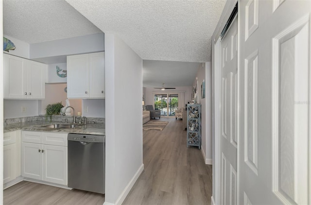 kitchen featuring white cabinets, light wood-style flooring, light stone countertops, stainless steel dishwasher, and a sink