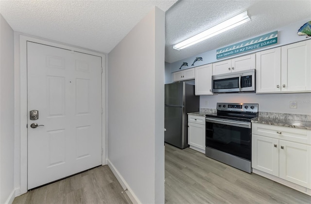 kitchen with a textured ceiling, stainless steel appliances, white cabinetry, baseboards, and light wood-style floors