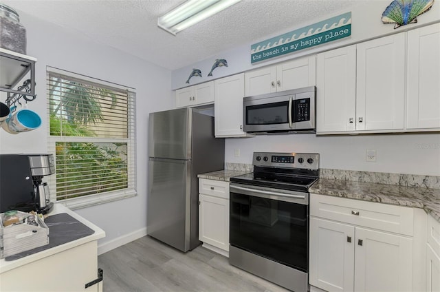 kitchen with light wood-style flooring, appliances with stainless steel finishes, white cabinets, a textured ceiling, and baseboards