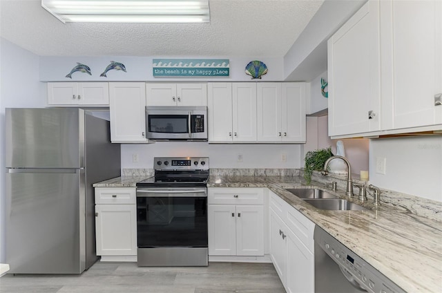 kitchen with light stone counters, appliances with stainless steel finishes, white cabinets, a sink, and a textured ceiling