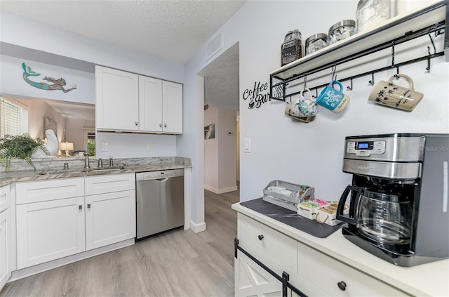 kitchen featuring a textured ceiling, light wood-style flooring, a sink, white cabinets, and dishwasher