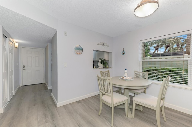 dining room featuring light wood-type flooring, a textured ceiling, and baseboards