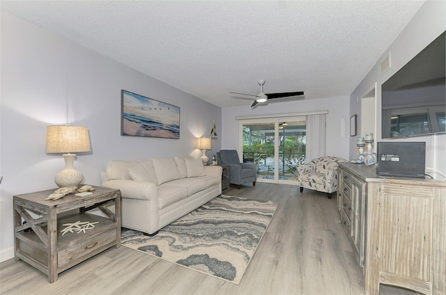 living area featuring a ceiling fan, visible vents, a textured ceiling, and wood finished floors