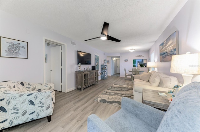 living room with a textured ceiling, ceiling fan, visible vents, baseboards, and light wood finished floors