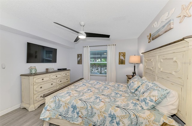 bedroom with a ceiling fan, light wood-type flooring, a textured ceiling, and baseboards