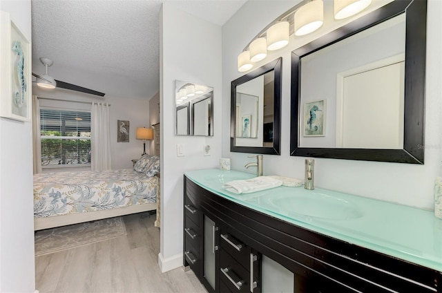 ensuite bathroom featuring a textured ceiling, wood finished floors, a sink, double vanity, and ensuite bath