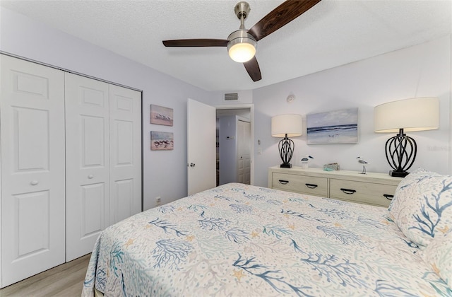 bedroom featuring a textured ceiling, light wood-style flooring, visible vents, a ceiling fan, and a closet