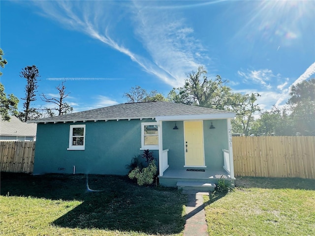 view of front of house featuring a shingled roof, a front yard, fence, and stucco siding