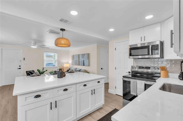 kitchen with visible vents, light wood-style flooring, stainless steel appliances, light countertops, and backsplash