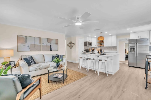 living room featuring a ceiling fan, recessed lighting, baseboards, and light wood finished floors