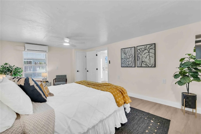 bedroom with an AC wall unit, wood finished floors, a ceiling fan, and baseboards