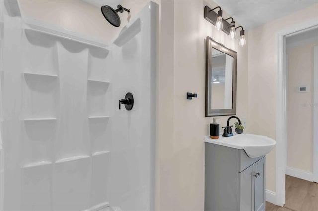 bathroom with a shower, wood finished floors, vanity, and baseboards