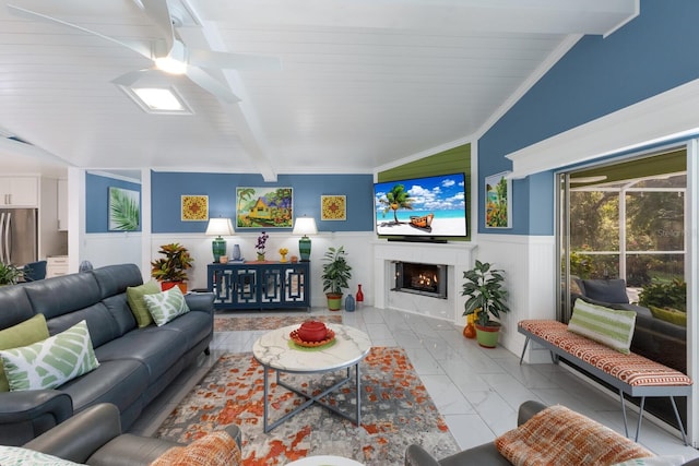 living room with lofted ceiling with beams, a wainscoted wall, marble finish floor, a lit fireplace, and crown molding