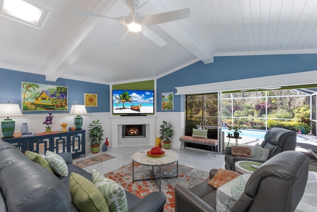 living room featuring a ceiling fan, a wainscoted wall, a sunroom, vaulted ceiling with beams, and a lit fireplace