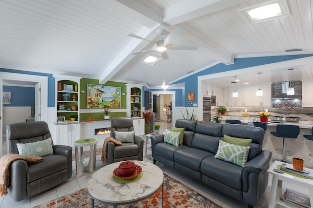 living area with light tile patterned floors, lofted ceiling with beams, a wainscoted wall, a ceiling fan, and a lit fireplace