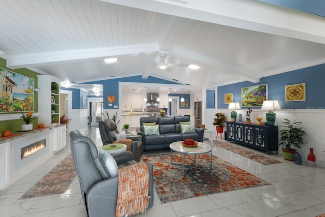 living area with a warm lit fireplace, wainscoting, wooden ceiling, and lofted ceiling with beams