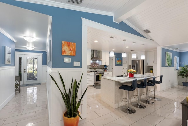 kitchen featuring stainless steel appliances, wall chimney range hood, wainscoting, and visible vents