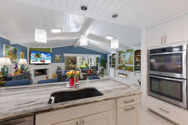 kitchen with a warm lit fireplace, light stone counters, a sink, open floor plan, and appliances with stainless steel finishes