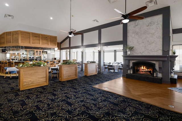 living room featuring a ceiling fan, a warm lit fireplace, visible vents, and a high ceiling