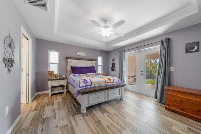 bedroom featuring a tray ceiling, light wood finished floors, access to exterior, and french doors