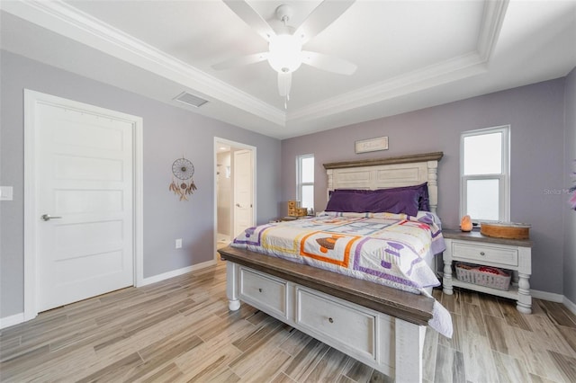 bedroom with multiple windows, a raised ceiling, and light wood-style flooring