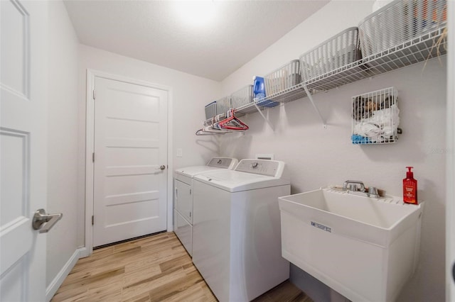 laundry area with washing machine and clothes dryer, light wood finished floors, baseboards, laundry area, and a sink