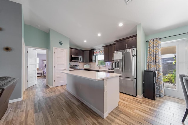 kitchen featuring a center island, dark brown cabinetry, appliances with stainless steel finishes, light countertops, and vaulted ceiling