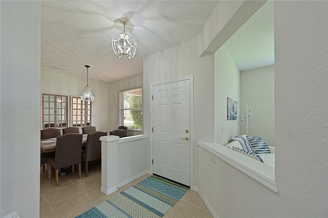 foyer featuring a textured wall, a notable chandelier, baseboards, and light tile patterned floors