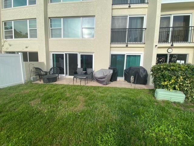 rear view of house with a yard, a patio area, fence, and stucco siding