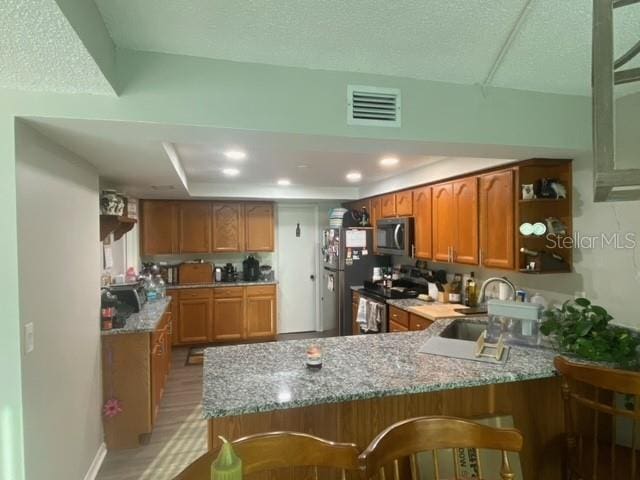 kitchen featuring stainless steel appliances, a peninsula, a sink, visible vents, and open shelves