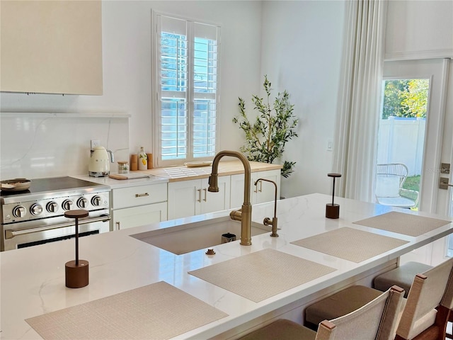 kitchen featuring stainless steel range, white cabinets, a breakfast bar area, light stone countertops, and a sink