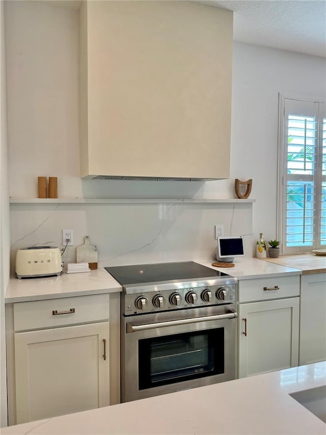 kitchen with a textured ceiling, light countertops, high end stainless steel range oven, and white cabinets