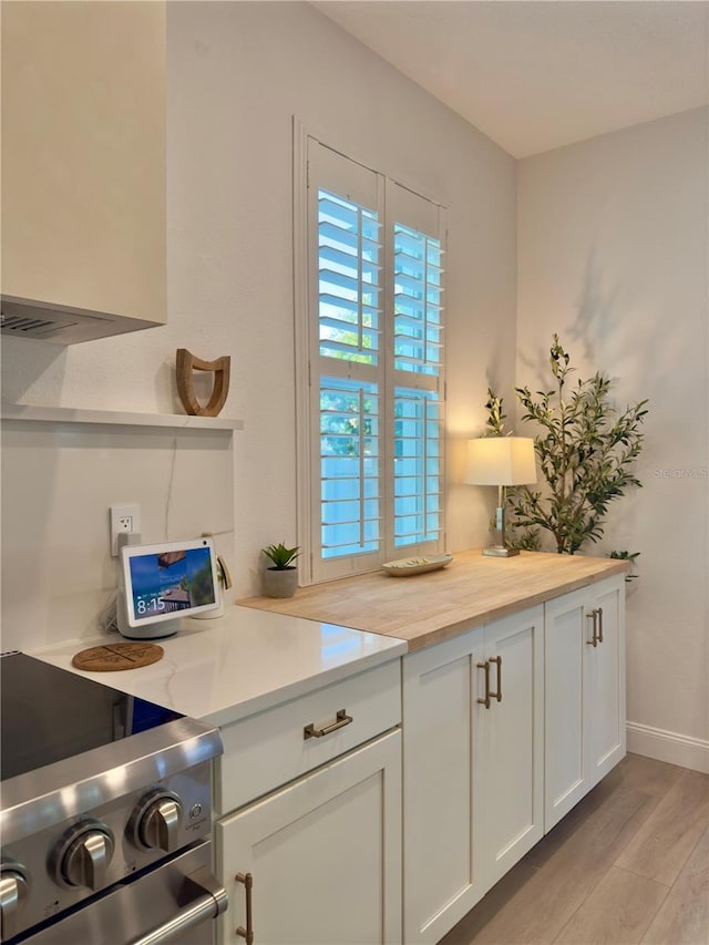 kitchen featuring stainless steel stove, white cabinetry, baseboards, and light wood finished floors