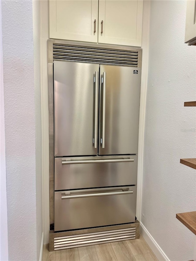 details featuring a textured wall, high quality fridge, light wood-style flooring, baseboards, and white cabinets