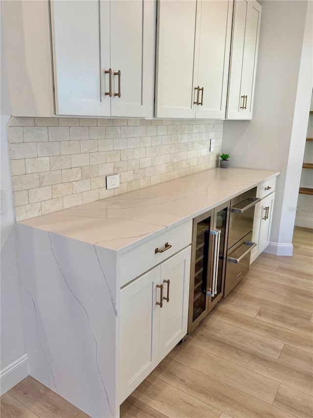 kitchen with light wood finished floors, beverage cooler, decorative backsplash, light stone counters, and white cabinetry