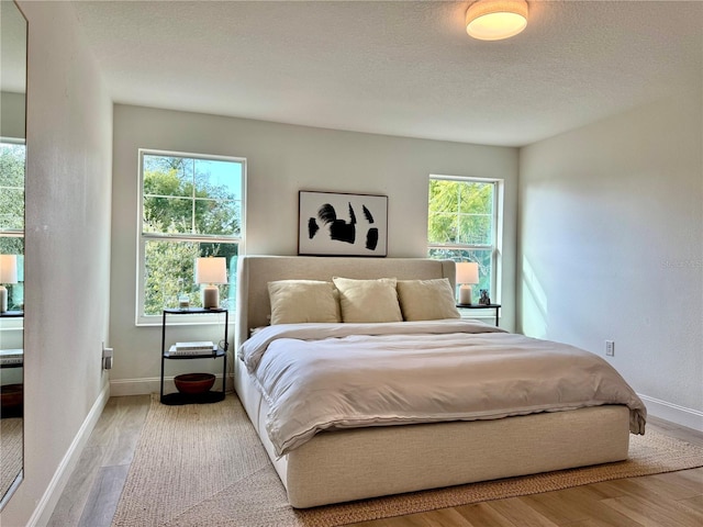 bedroom with a textured ceiling, baseboards, and wood finished floors