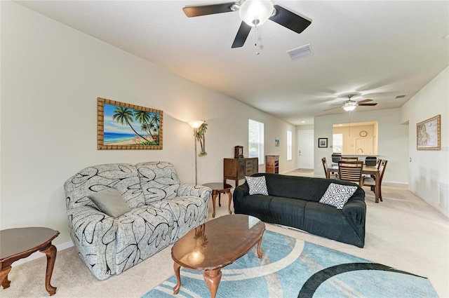 living room featuring baseboards, ceiling fan, visible vents, and light colored carpet