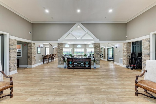 living area featuring a towering ceiling, light wood-type flooring, decorative columns, and visible vents