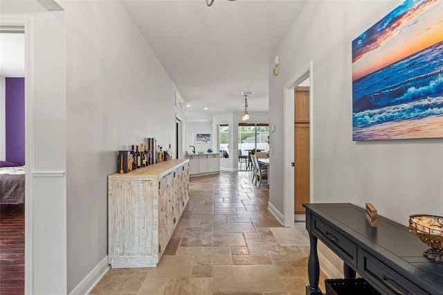 hall featuring baseboards and stone tile floors